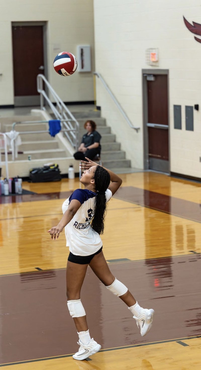 Arielle Akinwumi, number 9 in white, reaching overhead to serve