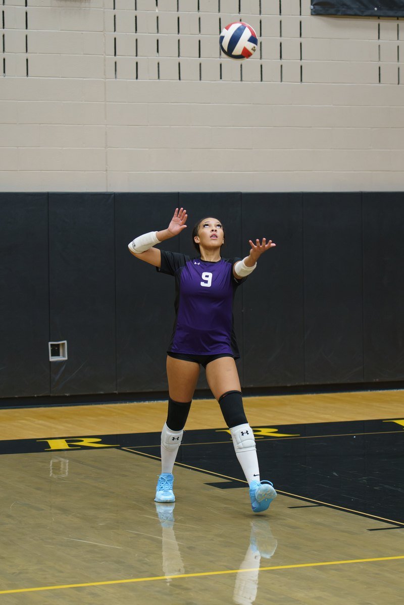 Arielle Akinwumi, number 9 in purple, watching the ball after her service toss